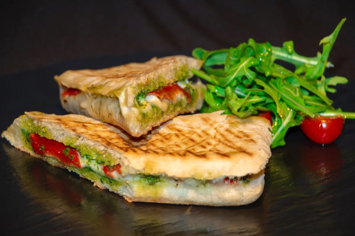 A grilled sandwich with green leaves and a half cherry tomato by its side.