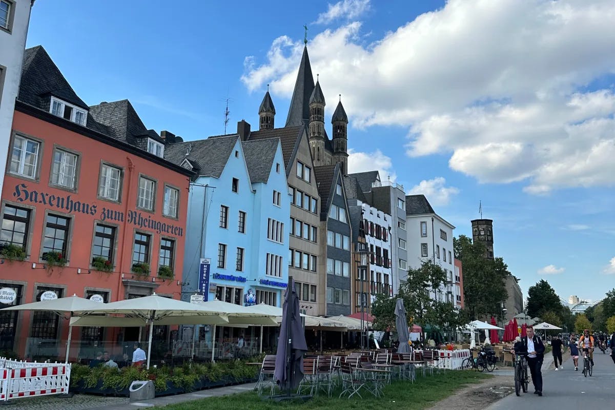 Colorful townhouses on a street with outdoor restaurant patios and chairs in Cologne