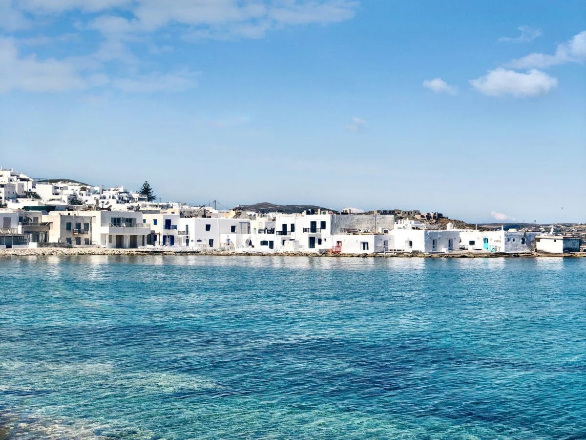 A scenic view of white buildings by a clear blue sea under a partly cloudy sky.