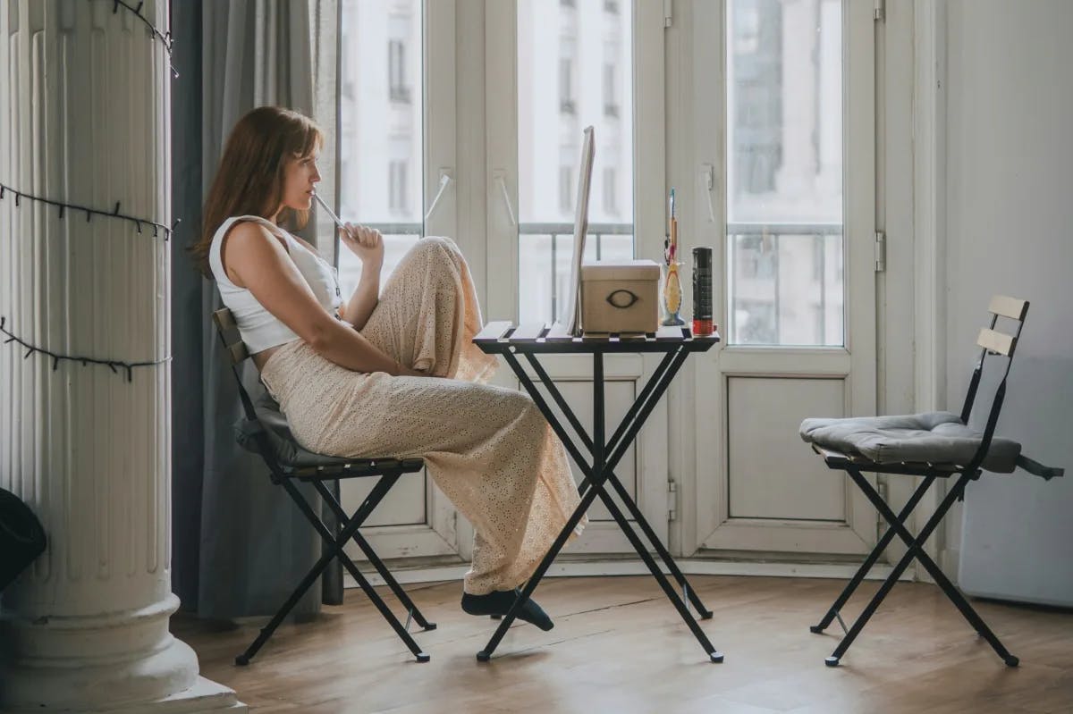 woman sitting at small desk thinking in front of a window