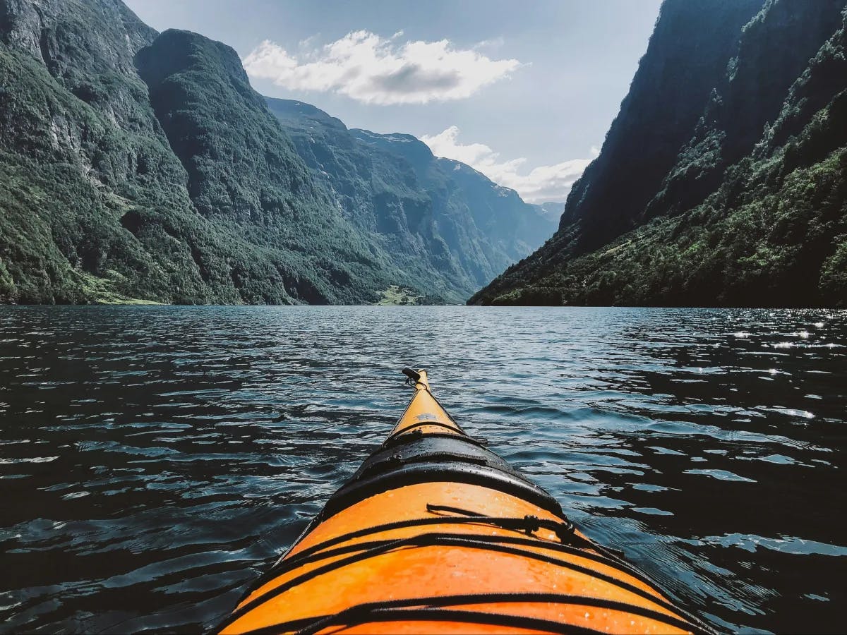 person-in-orange-kayak-in-lake-surrounded-by-hills-Norway-travel-guide