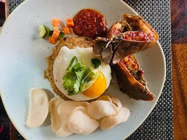 The image presents a plated meal featuring lobster tail, fried egg, rice, crackers, and diced vegetables.