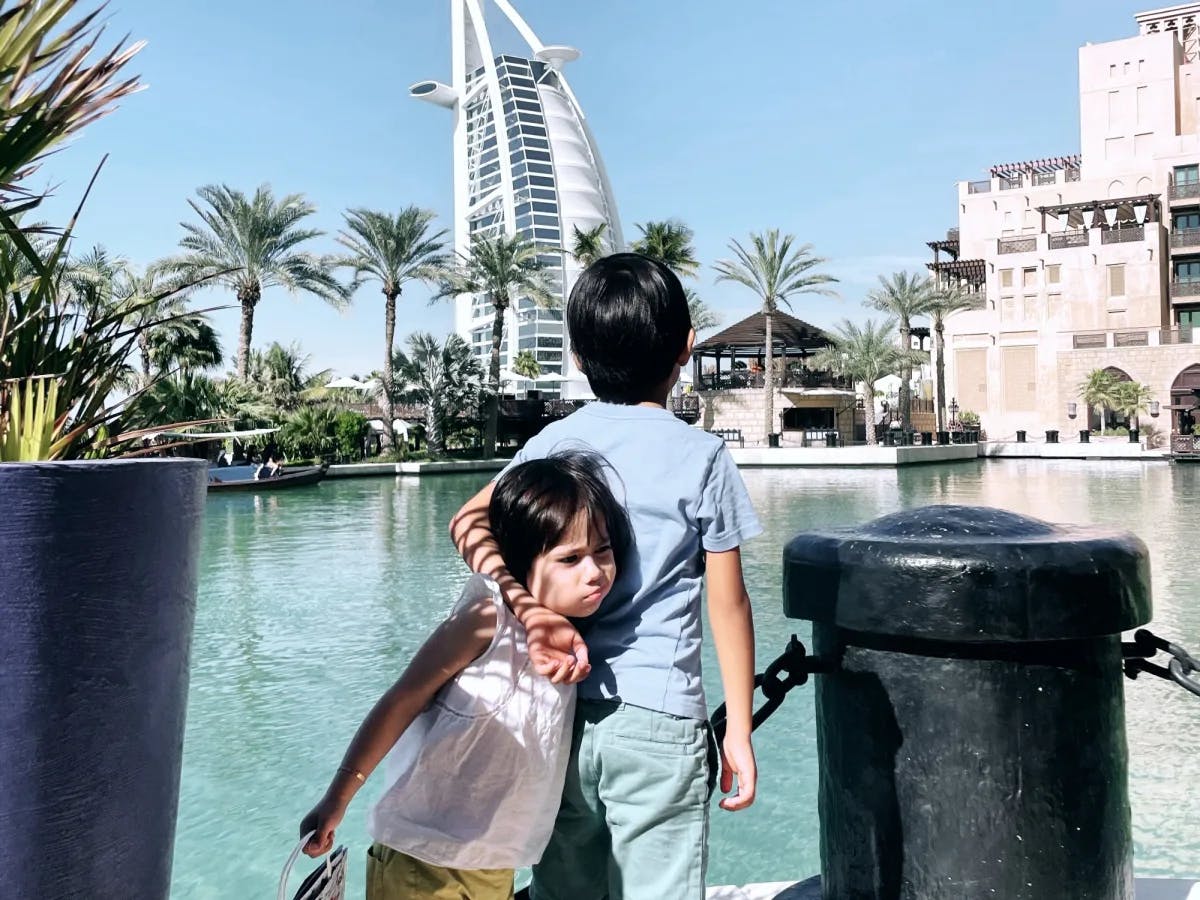 Two kids in front of a water body and a white tower. 