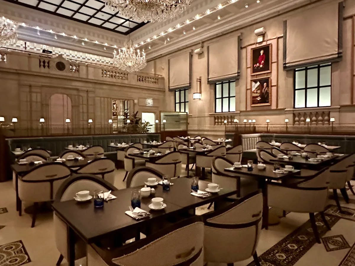 An elegant dining area with ornate chandeliers, a patterned floor and tables set for service.