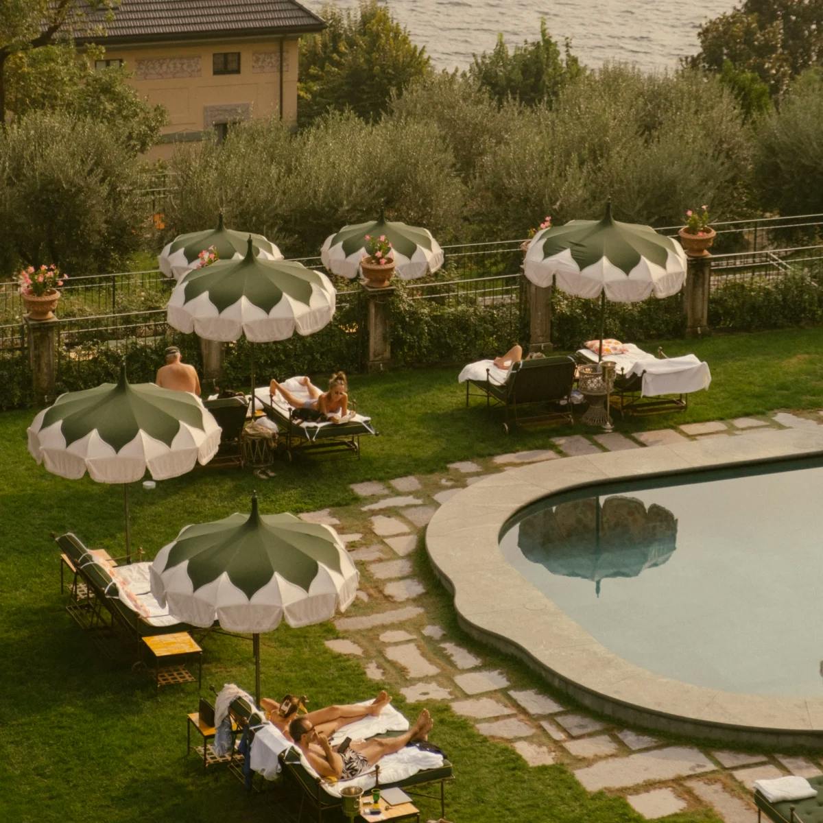 aerial view of people lounging by a pool surrounded by grass and green umbrellas