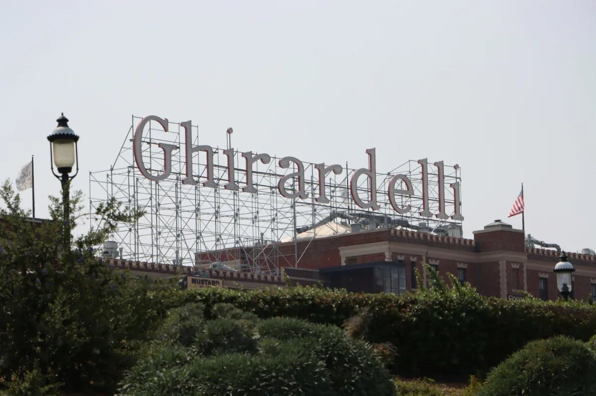 A brown and white building and Ghirardelli written on steel towers.