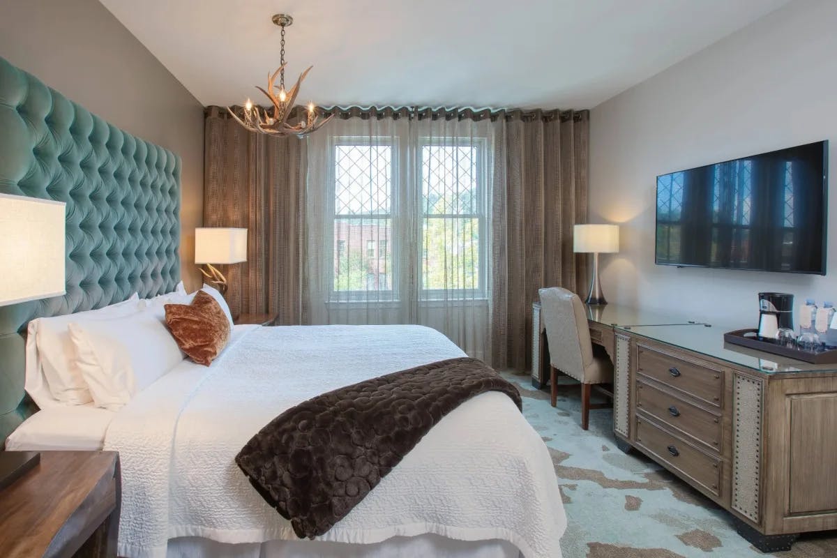 stylish hotel room with a white bed an antler chandelier and desk with tv