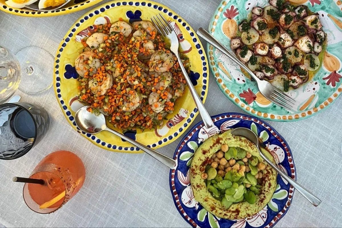 Colorful plates of food on a table next to an Aperol spritz.