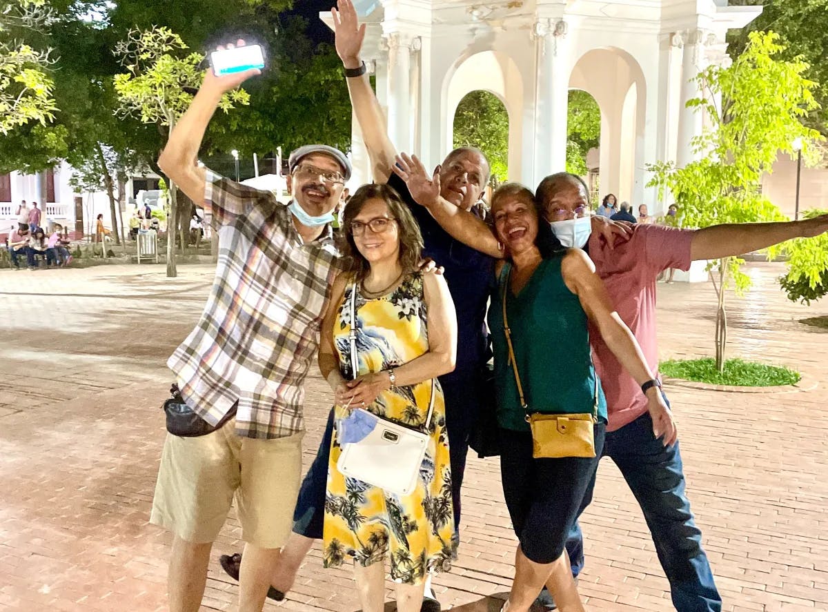 A lively group strikes a pose with uplifted arms in front of a nighttime gazebo, faces whimsically concealed.