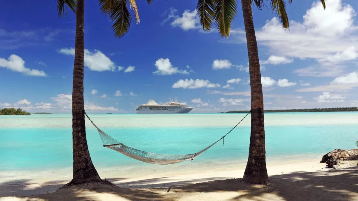 Two palm trees with a swing in between on the blue water beach.