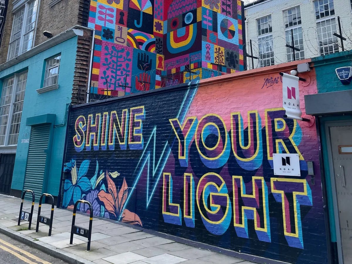 A colorful mural on a brick wall that reads "shine your light"