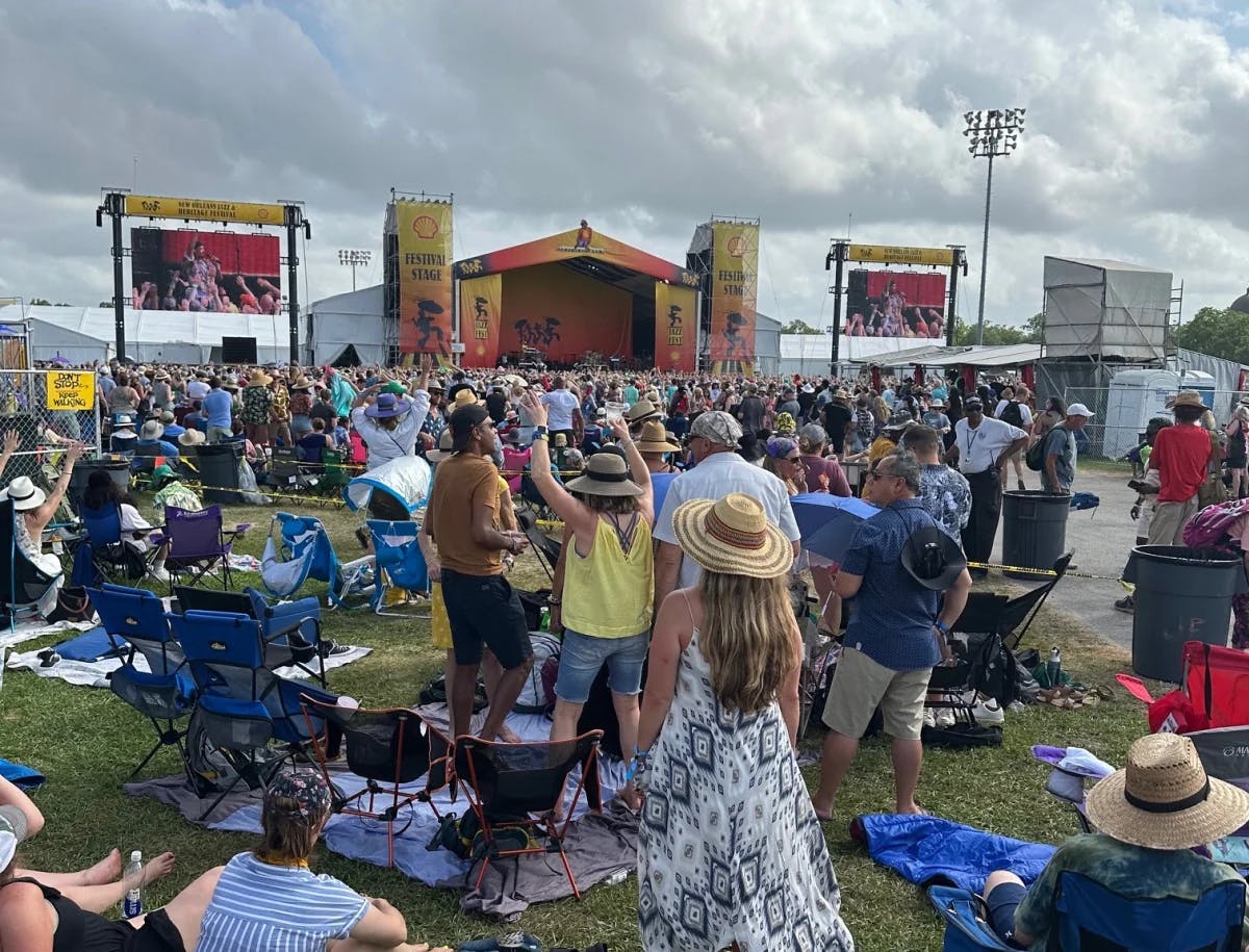 A bustling outdoor gathering with attendees seated and focused on a stage during daylight.