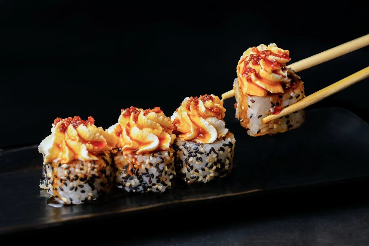 Four sushi rolls in a black tray with chopsticks