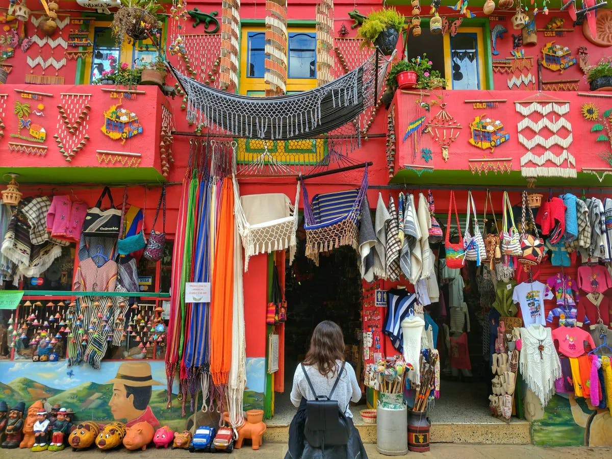 A colorful storefront displaying a variety of traditional textiles and crafts, with a person standing in front, immersed in the vibrant scene.