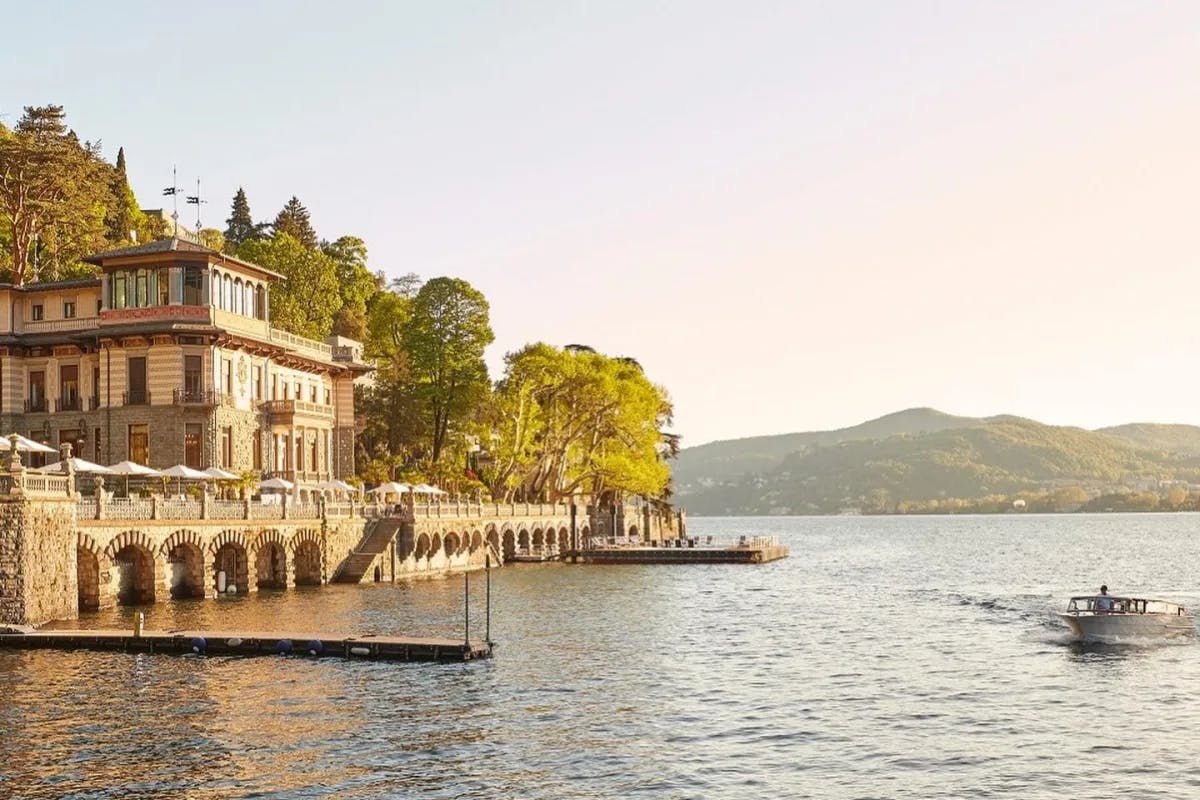 A view of the stunning Mandarin Oriental, Lago di Como Hotel with a sailing boat, mountains in the background, right before dusk.