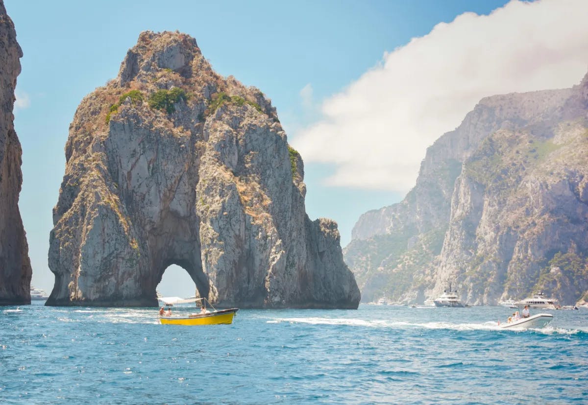 Boats near arch-shaped rock formations and cliffs on a sunny day.