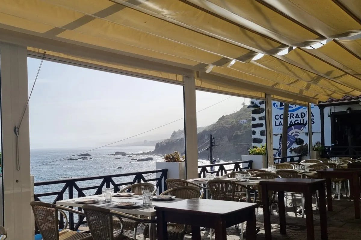 A seaside covered restaurant patio at Cofradía Las Aguas with wooden tables overlooking the ocean.