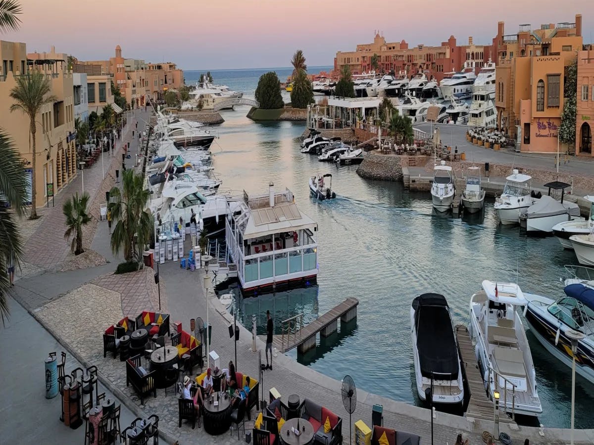 An aerial view of the Marina sunset from Captain's Inn complete with tourists, boats anchored in a harbor and buildings around the water.