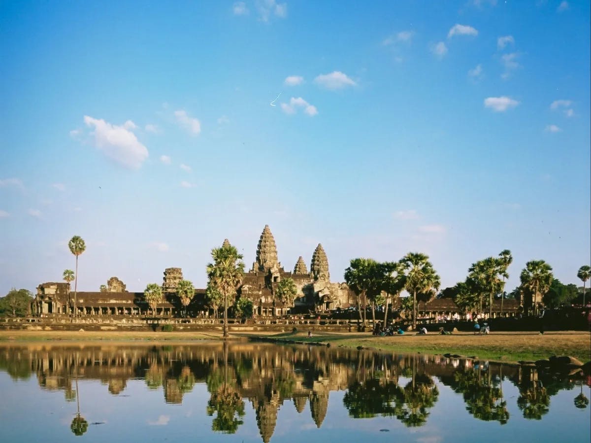 A picture of a huge golden-colored temple near the water taken during the daytime.