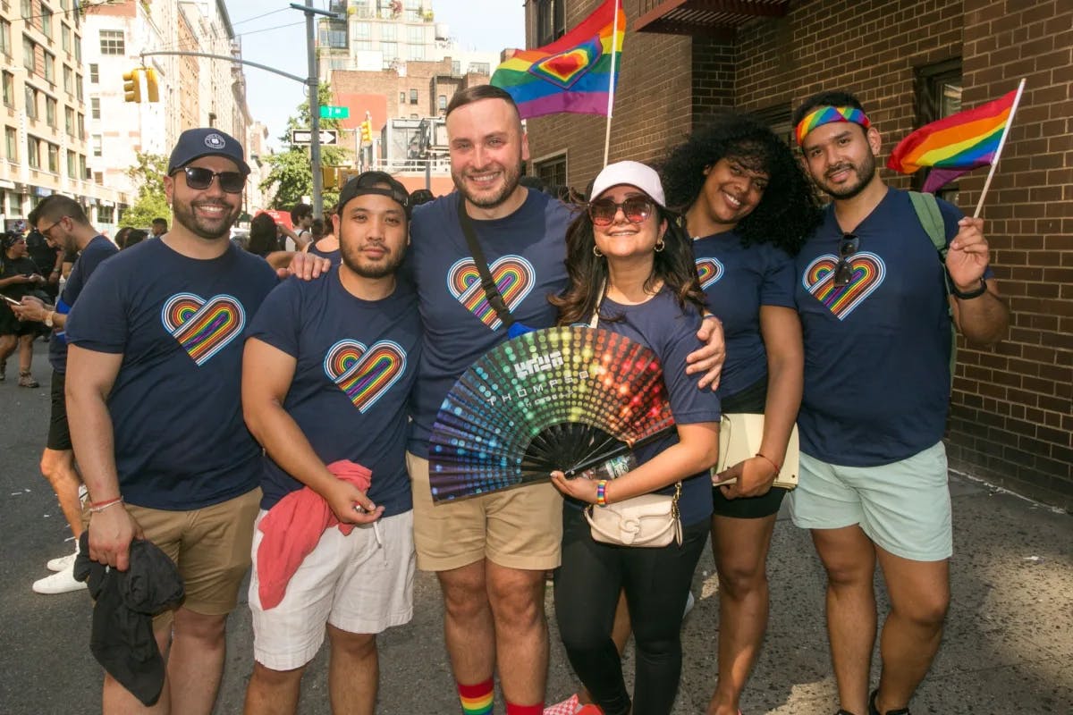 group of six adults wearing navy rainbow heart t-shirts waving rainbow flags