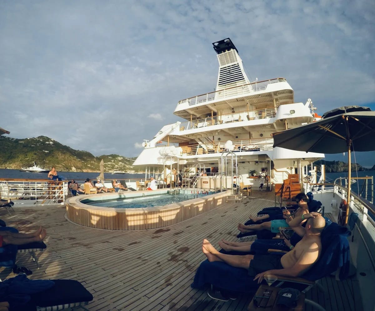 Deck of the ship with pool and lounge chairs with cliffs in the background.