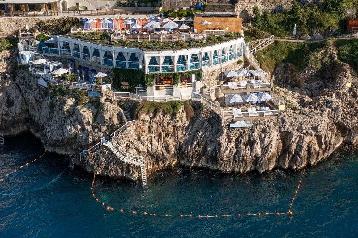 aerial shot of a hotel perched on a cliff over blue sea