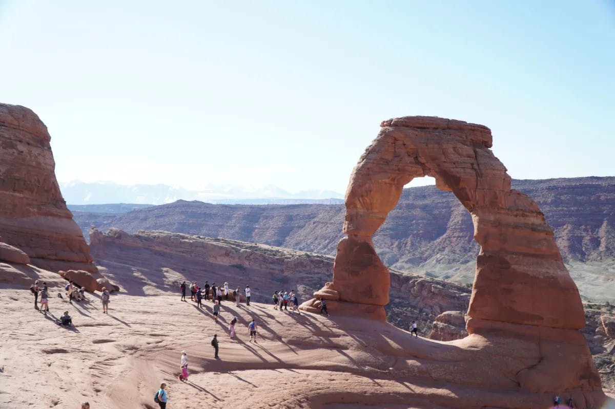 Big rock structure with a hole surrounded by people.