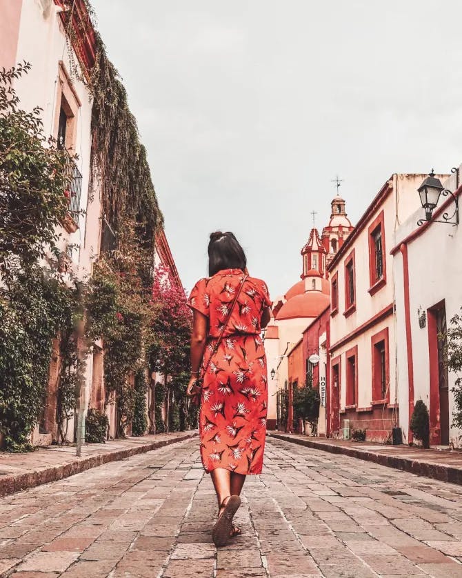 View of advisor in a long red dress walking in the center of a cobblestone street lined with colorful buildings