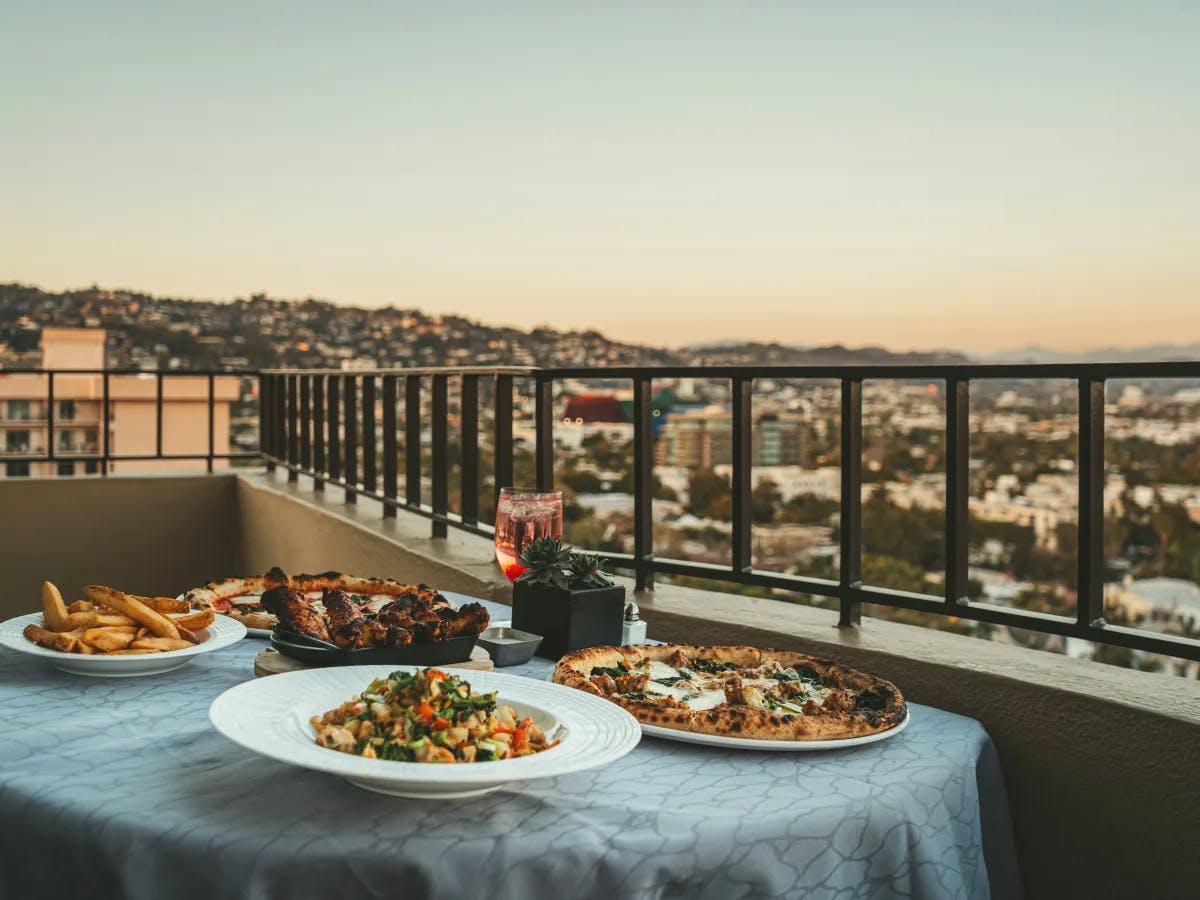 The image presents a cozy balcony dining setup with a view of the city’s evening lights.