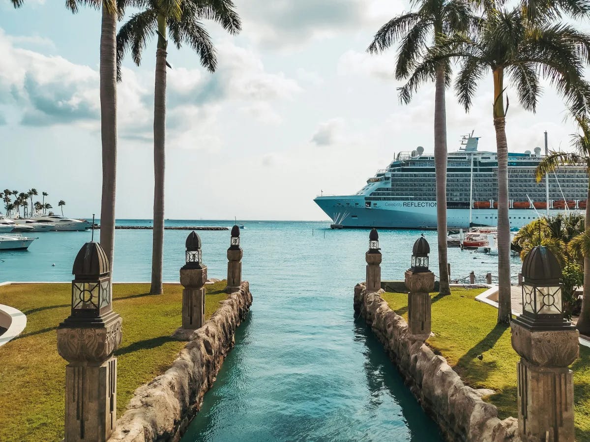 A cruise ship docked at a tropical port, adorned with palm trees and ornate lamp posts.