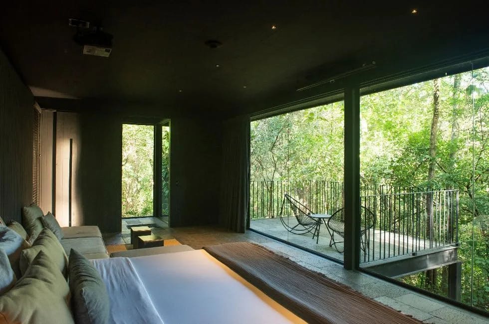 a sleek hotel rom in the jungle with floor-to-ceiling windows and a polished concrete floor