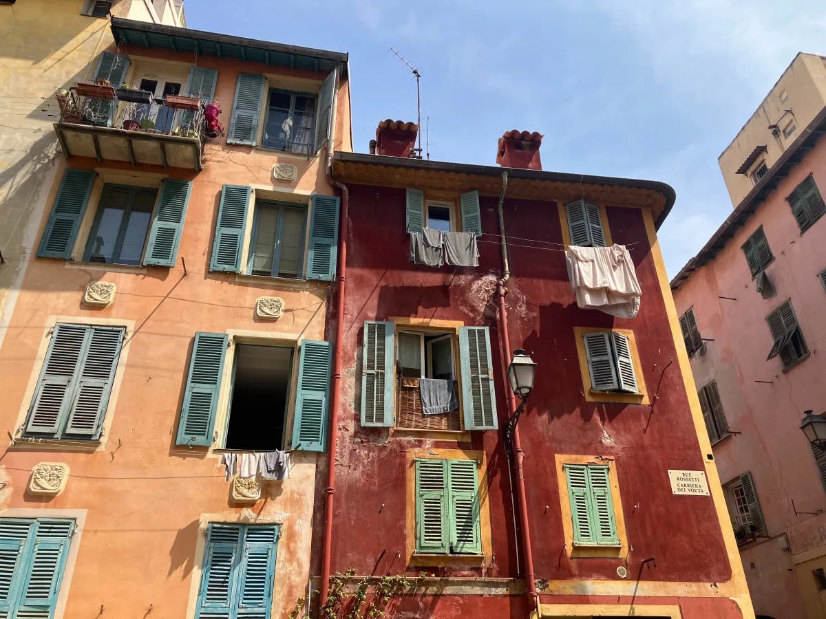 A quaint, weathered building facade with green shutters and laundry drying, evoking a charming European atmosphere.