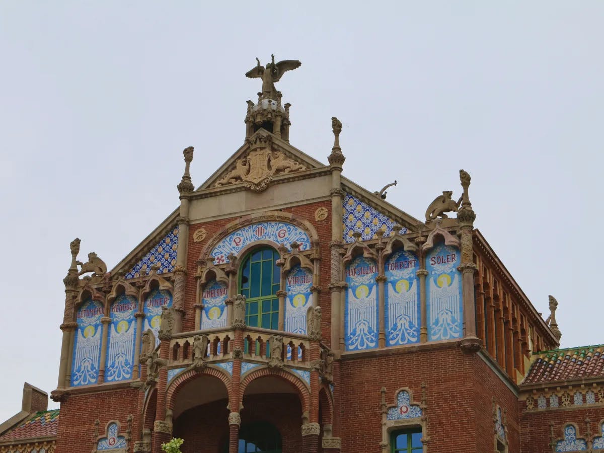 The image depicts a building with intricate architecture and decorative tiles under a cloudy sky.