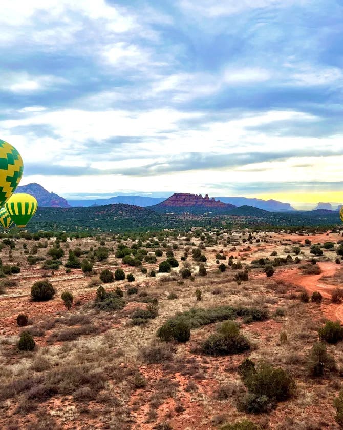 A view of colorful hot air balloons above the desert with a mountain in the background.