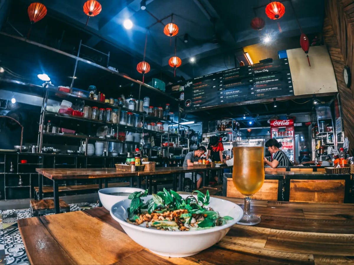 The image shows the interior of a restaurant with Asian-inspired decor, featuring red lanterns and a bar area with shelves of bottles.