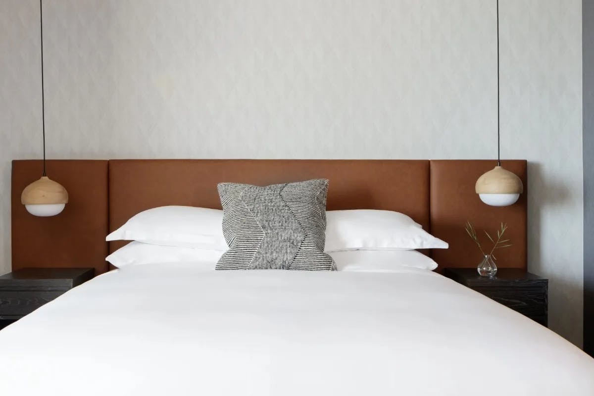 white bed with leather headboard flanked by modern hanging lights