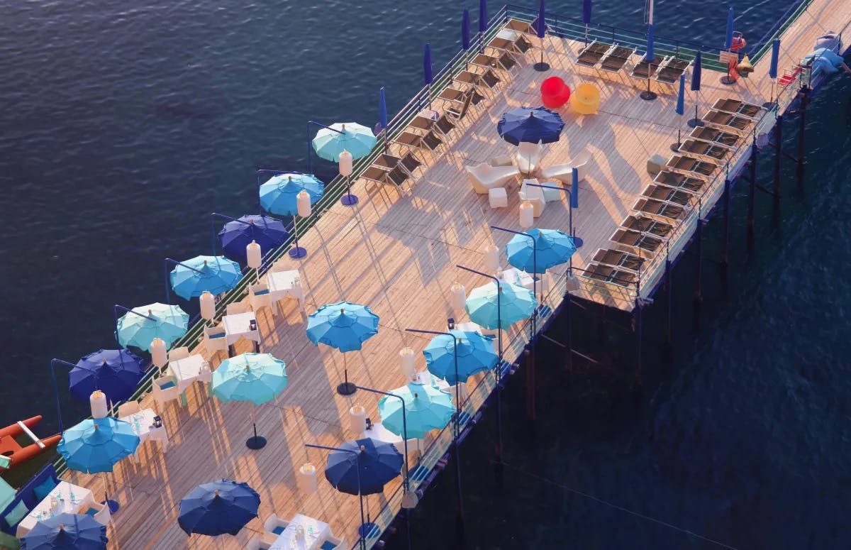 A deck in the ocean with blue umbrellas and sun loungers