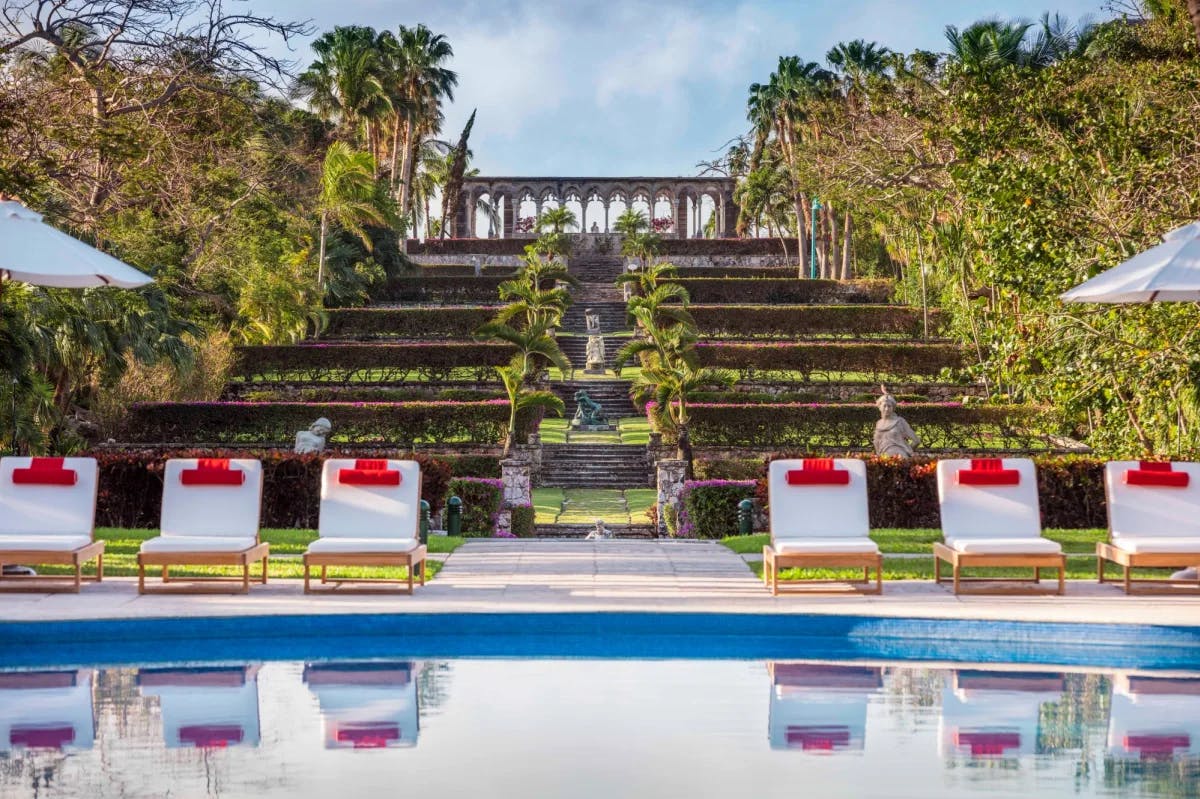 blue pool surrounded by cushioned lounge chairs with stone stairs in the background