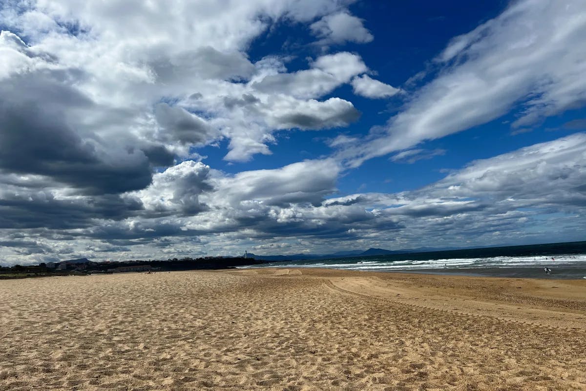 A large swath of sandy beach under a vast blue sky with clouds.