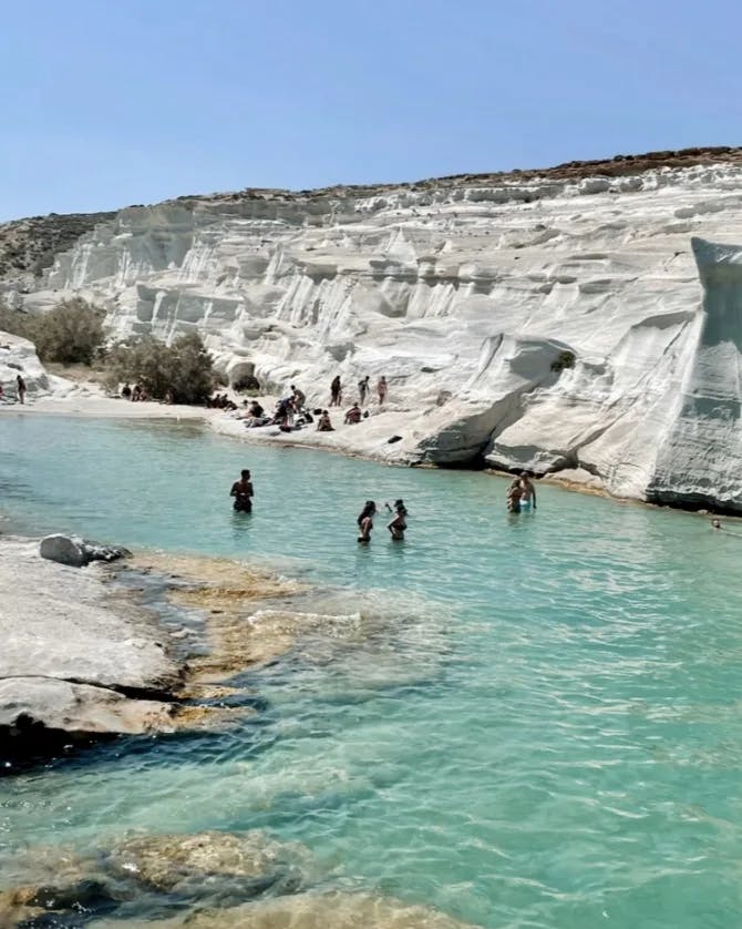 People swimming in a turquoise lake surrounded by white rocks and clear blue skies