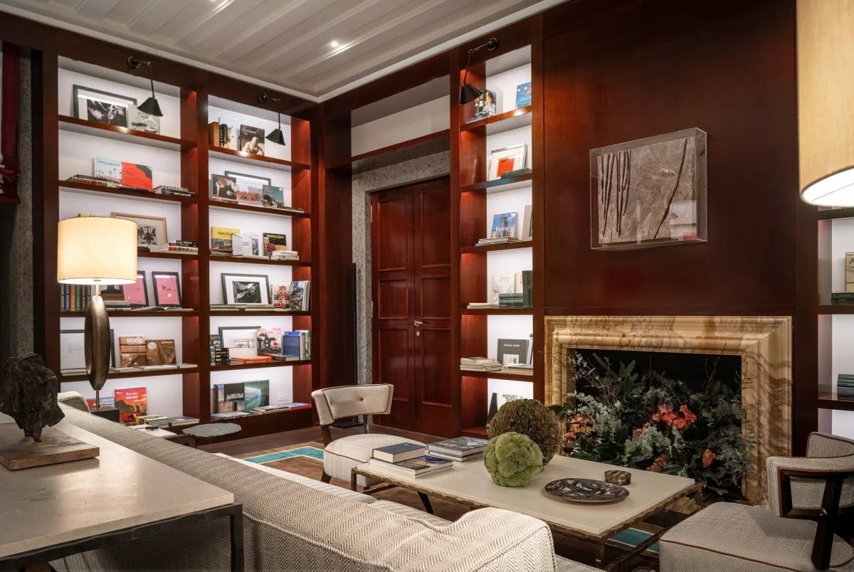 a luxe living room with a plant-filled marble fire place and floor-to-ceiling shelves housing picture frames and books