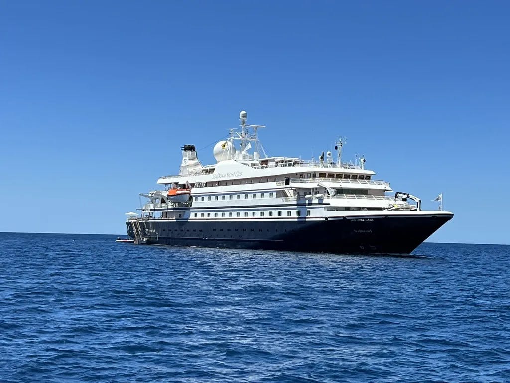 The white SeaDream ship from afar on the ocean on a clear day.