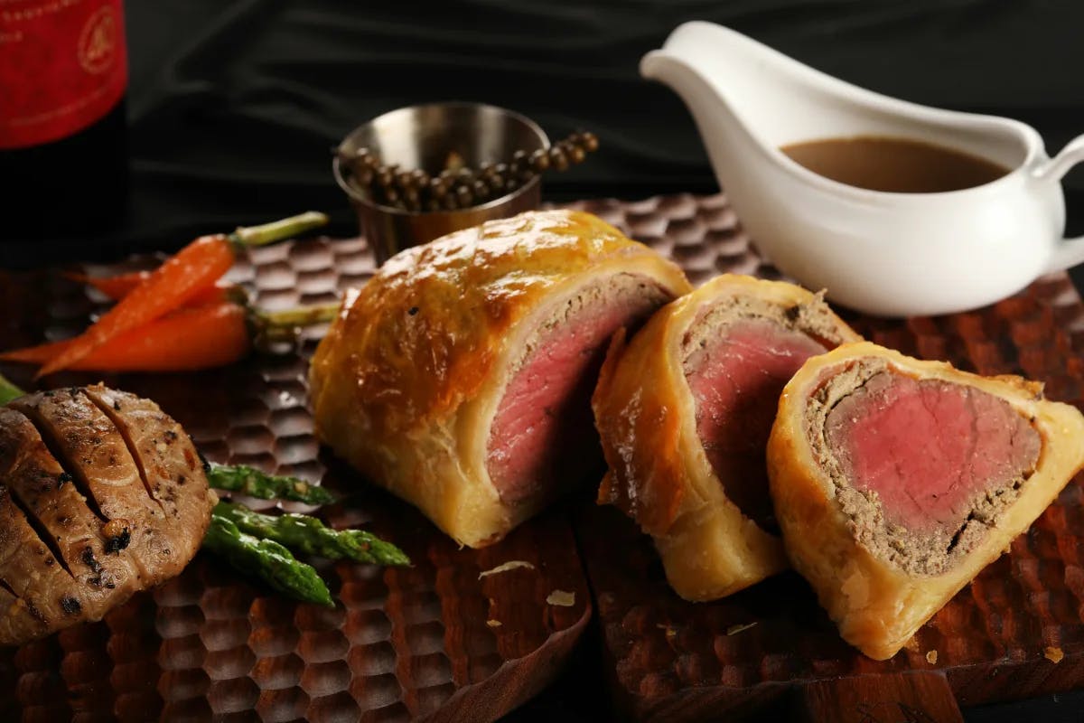 A plate of beef Wellington, with red-centered steak wrapped in pastry next to a gravy boat.