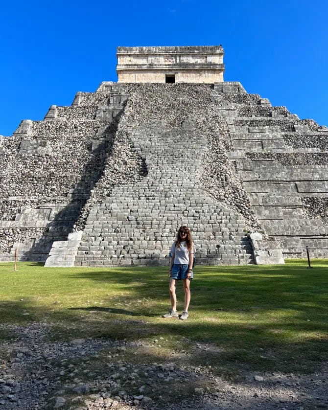 Kayla standing alone on the grass in front of an ancient pyramid under clear skies