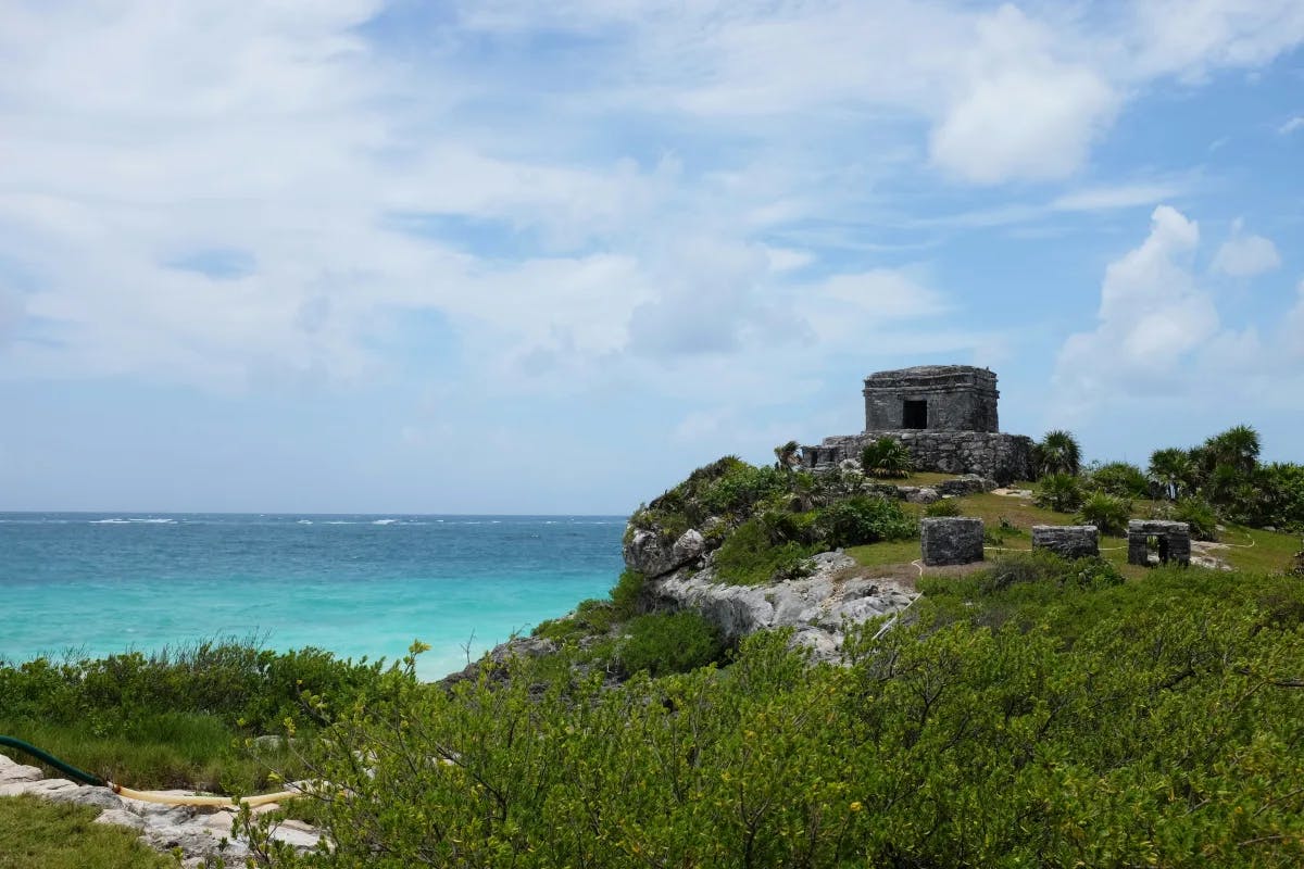 Tulum ruins on a green hill overlooking the ocean.