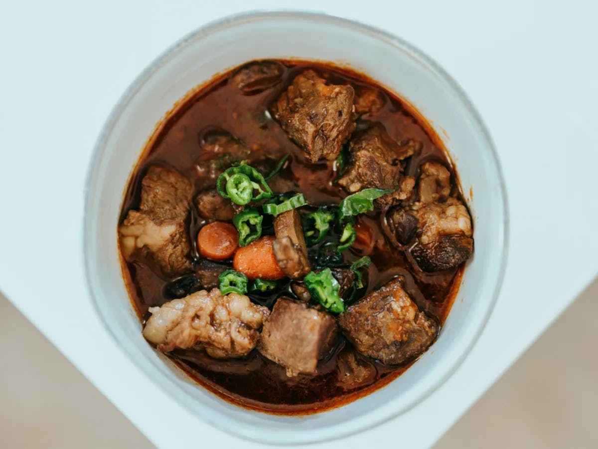 An above and close-up shot of a traditional meat stew with vegetables in a dark broth.