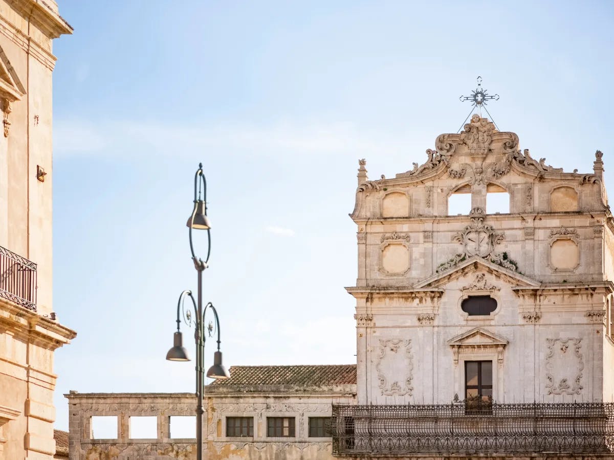 The image shows an ornate, historical building facade under a clear blue sky, with a street lamp in the foreground.