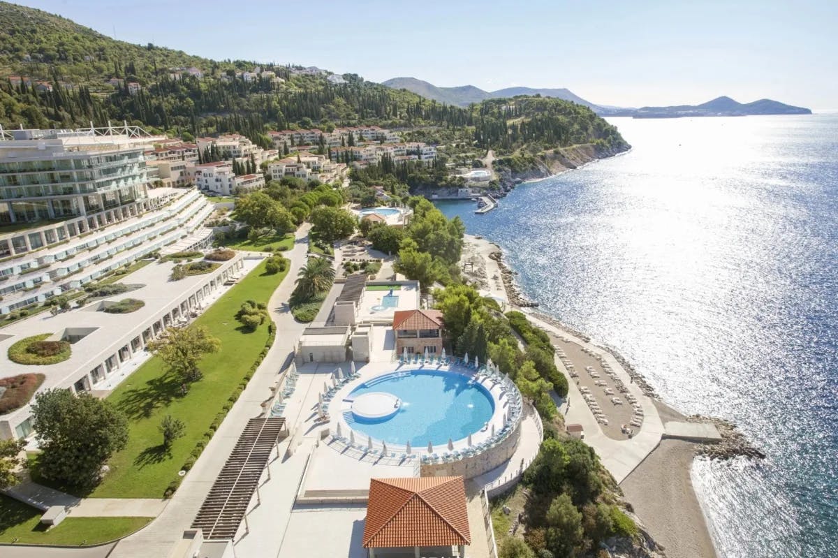 large resort with green lawn and round pool overlooking the sea