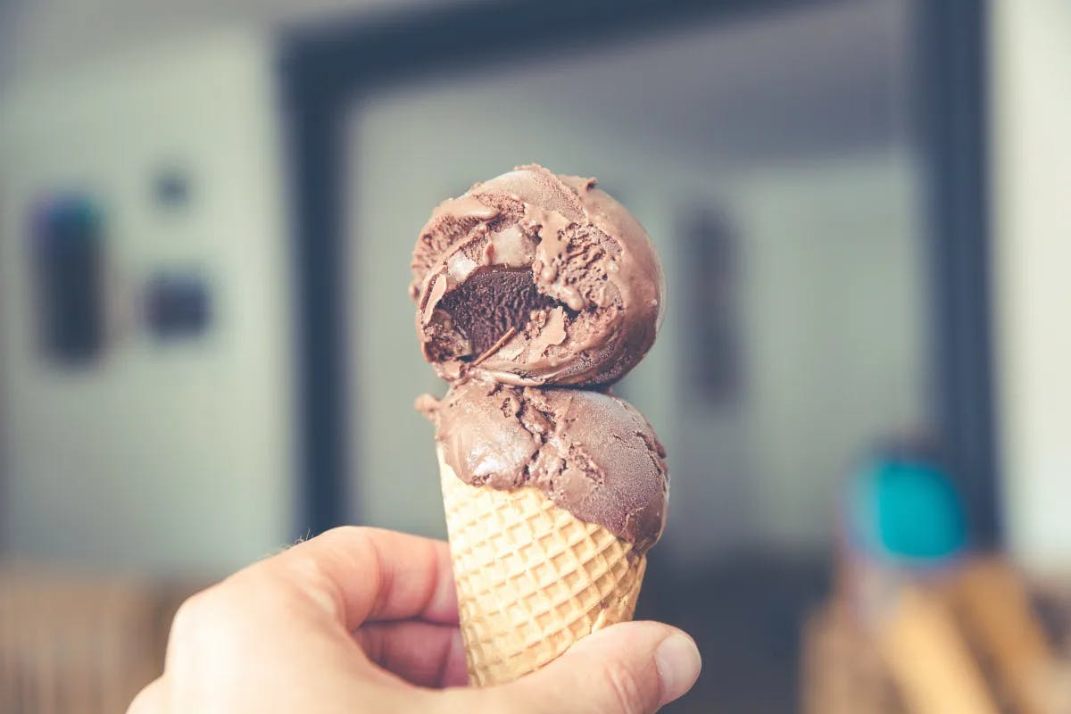 A hand holding an ice cream cone with two scoops of chocolate ice cream.