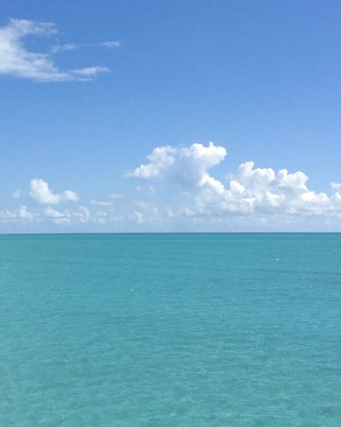 A calm blue sea and blue sky with puffy clouds